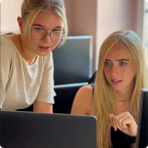 Zwei Kolleginnen sehen gemeinsam auf einen Laptop